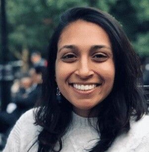 A smiling woman with medium-length brown hair, wearing a white sweater, with a blurred green background.
