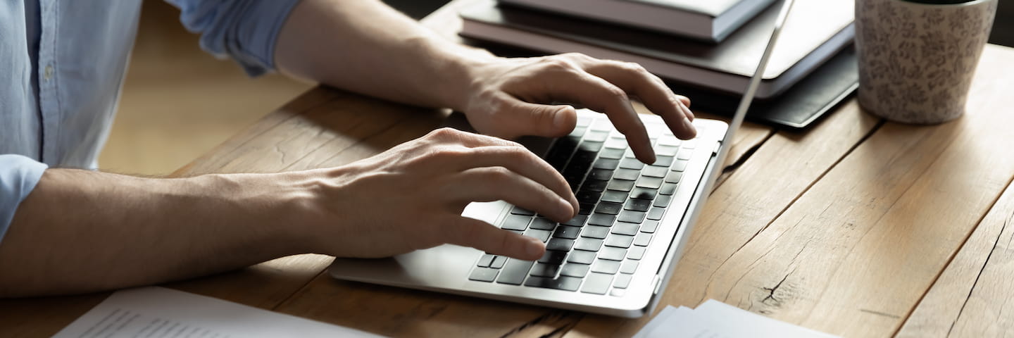 Close-up of a person's hands typing an advertising disclosure on a computer keyboard on a wooden desk, with documents and a coffee cup nearby.