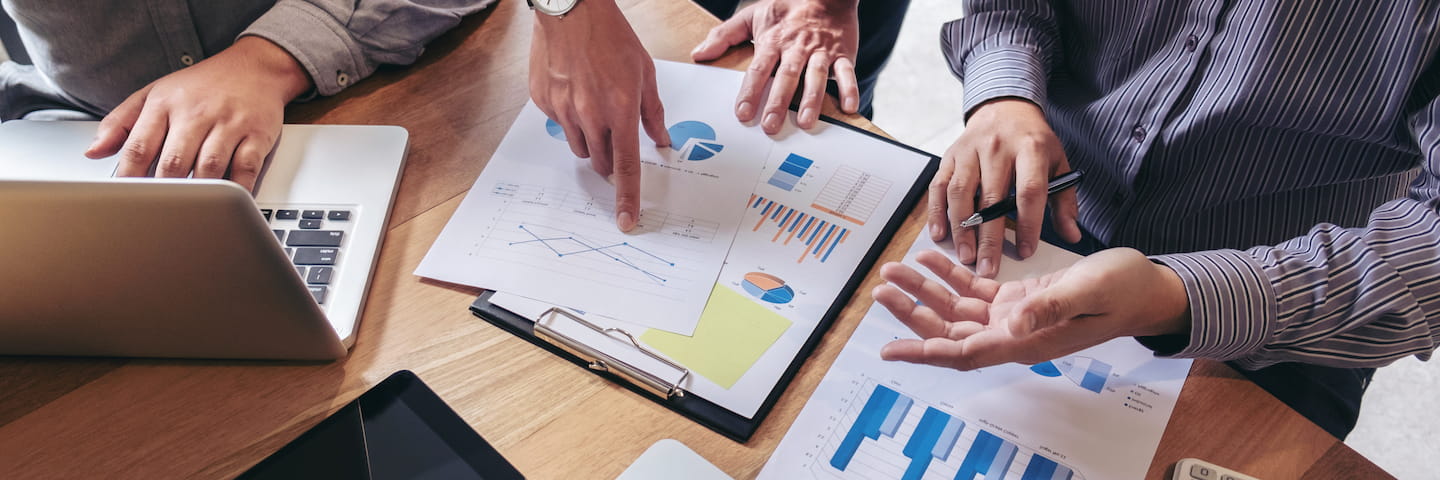 Three people discussing business strategies with charts, graphs on a table, and a laptop open beside them showcasing the best online accounting programs.