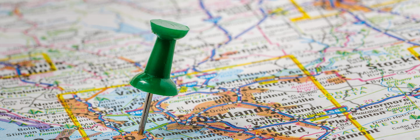 A green pushpin on a detailed road map, pinpointing a location in the Oakland area, with nearby city names and routes to colleges near you visible.