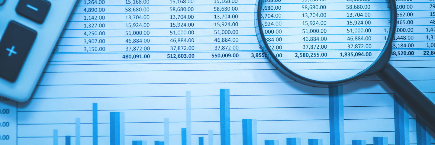 Magnifying glass focusing on forensic accounting data with a calculator beside it, highlighting detailed bar graphs and numerical statistics on a printed spreadsheet.
