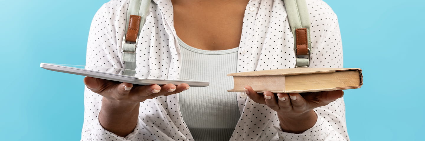 A woman holding a tablet in one hand and an old book in the other, comparing online MBA and traditional MBA reading methods, against a blue background.