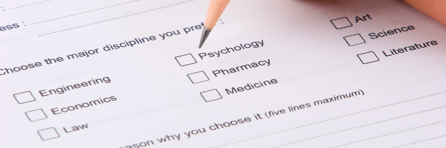 Close-up of a hand holding a pencil over a survey form that includes options to choose a college major such as engineering, psychology, science, and literature.
