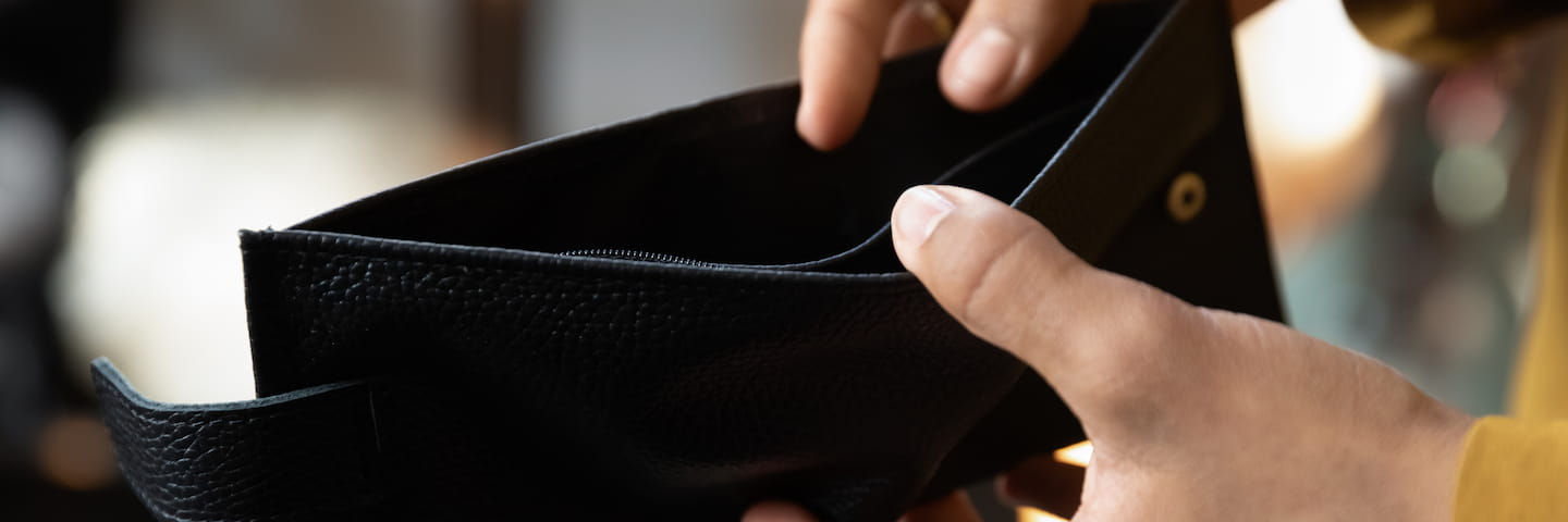Close-up of hands opening an empty black leather wallet, suggesting financial hardship or lack of money for low-income students.